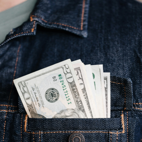 A stack of American dollar bills in a denim jacket pocket