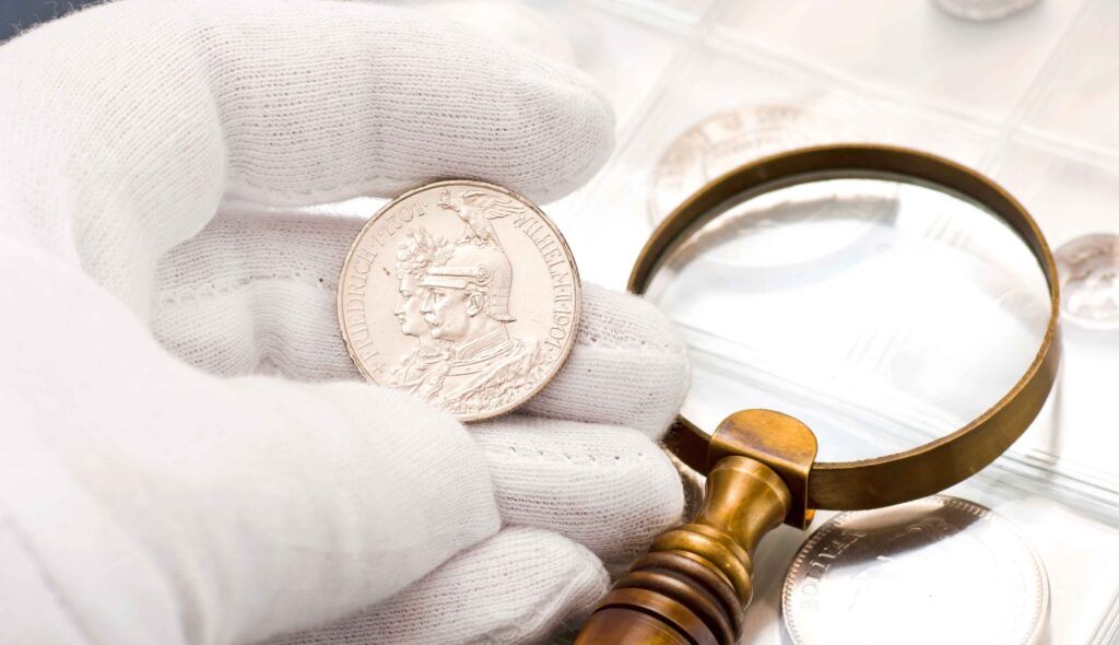  A man’s hand in a white glove holding a coin while deciding the value of a coin collection